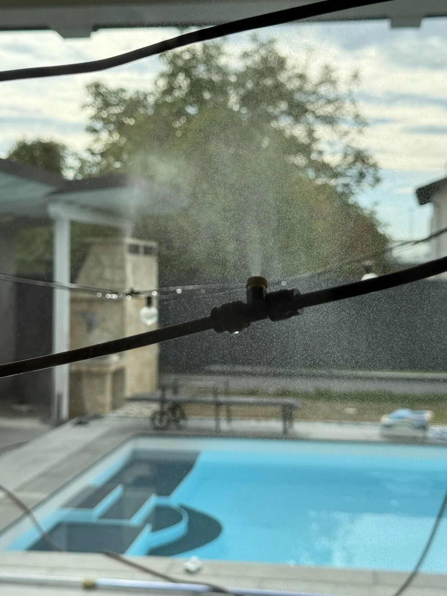 Sprühnebeldüse an einer schwarzen Leitung über der Terrasse, feiner Nebel tritt aus